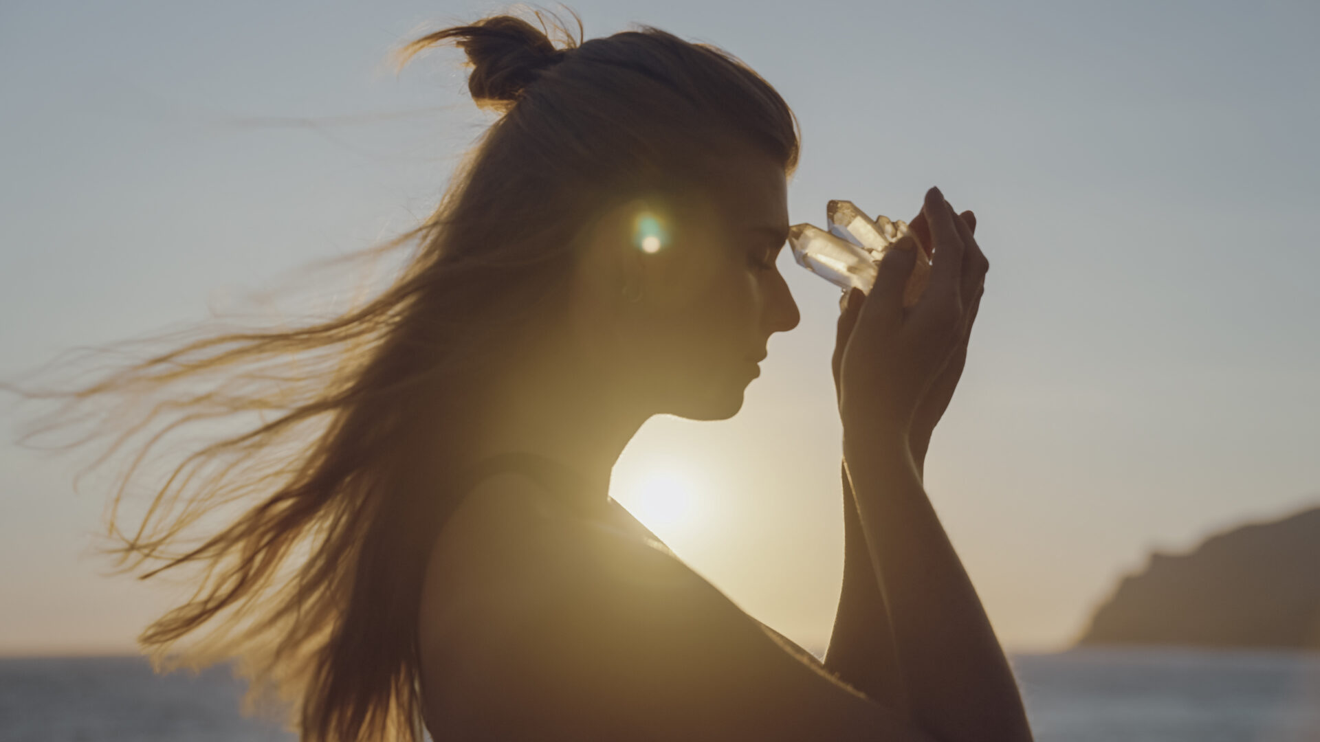 Woman holding crystal against sunset sky.
