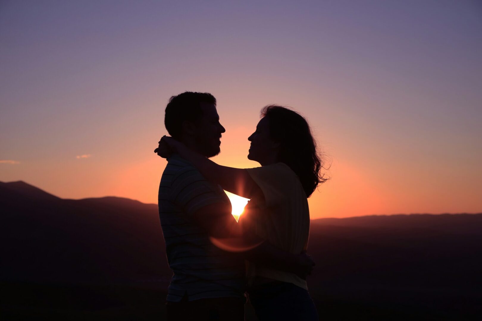 Couple embracing at sunset, silhouetted view.